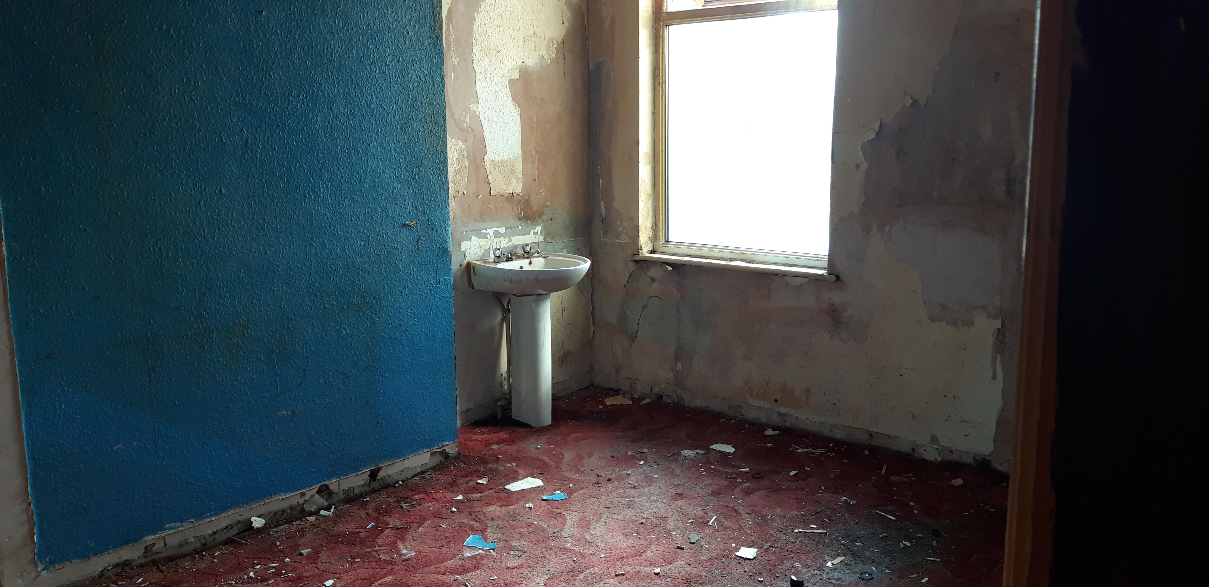 Dilapidated bathroom with peeling walls and rubble on the floor at acquisition